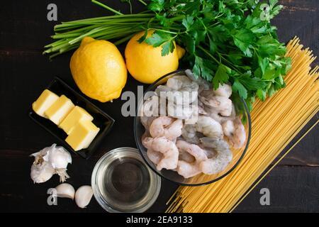 Garlic Butter Shrimp Pasta Ingredients: Peeled shrimp, lemons, spaghetti, and other ingredients on dark wood background Stock Photo