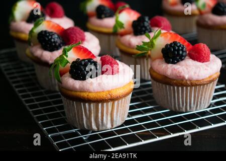 Lemon Cupcakes with Lemon Raspberry Buttercream Icing: Cupcakes decorated with pink frosting and fresh berries on wire cooling racks Stock Photo