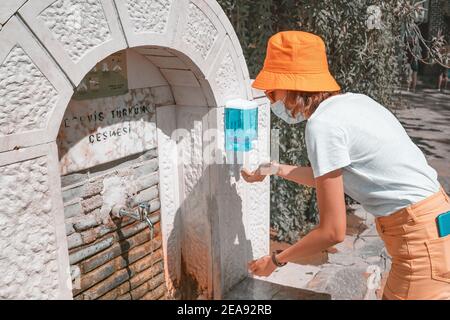 06 September 2020, Turkey, Antalya: Happy woman washes her hands at the city street in a spring fountain, using sanitizer and soup Stock Photo