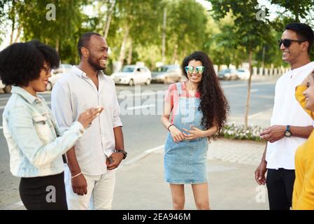 Young people having fun outdoors. A group of multi-ethnic friends are talking and laughing while standing in the street. Stock Photo