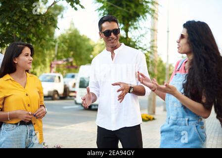 Young people having fun outdoors. A group of multi-ethnic friends are talking and laughing while standing in the street. Stock Photo