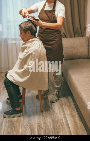 Woman cutting her elderly mother's hair at home. self isolation concept Stock Photo