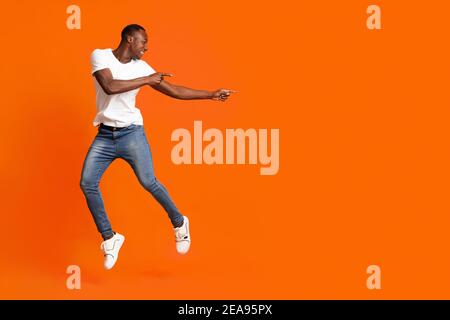 Millennial african american man pointing at copy space while jumping Stock Photo