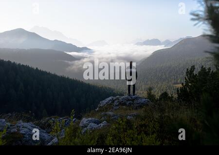 Hikers on rock before sunrise at Cinque Torri in the Dolomites, South Tyrol, Italy. In the valley there is a sea of fog, over which various mountain ranges extend Stock Photo