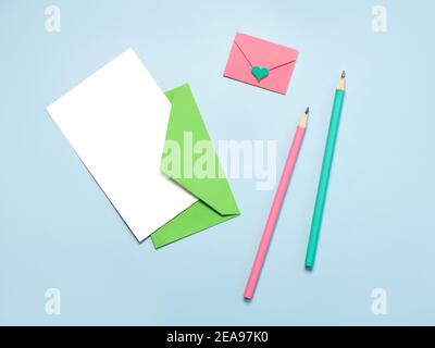 green paper envelope with white card, pink paper envelope pink and green pencils on blue background Stock Photo