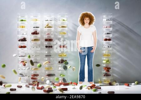 Woman in the midst of colorful tablets, in front of pill cans, white-gray background, studio, with jeans and white T-shirt, curly red hair