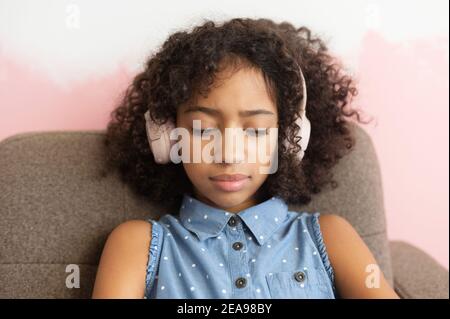 Upset African-American school-age girl looks down and feels offense. Difficult teen-age Stock Photo