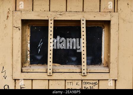 Aged garage door window newly painted with faint yellow paint with metal window bars scratches and writings Stock Photo