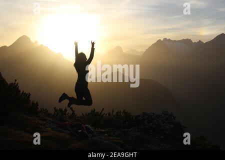 young woman jumping at sunset in the direction of Arnspitzen, Wetterstein Mountains, taken on Gamseck above the Mittenwalder Hut Stock Photo