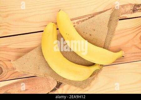 Two bright yellow ripe juicy organic bananas, on a jute napkin, against a background of natural wood. Stock Photo