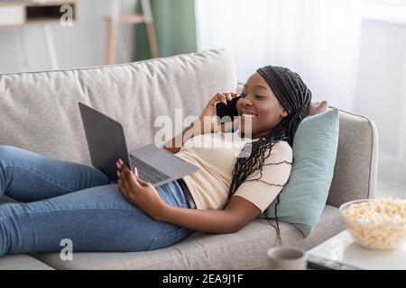 Happy black woman laying on couch with laptop and smartphone Stock Photo