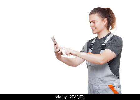 worker in gray uniform overalls holds a tablet mobile device for diagnostics and maintenance of electronic devices of a car, mechanic isolated on a wh Stock Photo