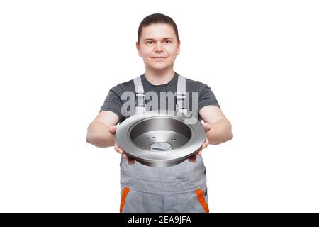 male mechanic in gray uniform holds brake disk in hands car spare parts of automobile brakes, shop sale of iron alloy product isolated on white backgr Stock Photo