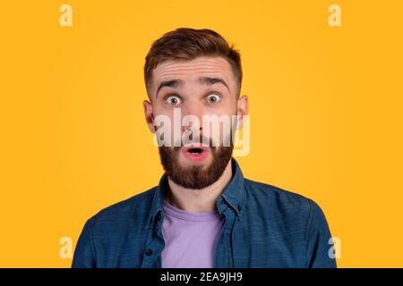 Unbelievable news. Portrait of bearded young guy opening mouth and eyes in shock, looking at camera on orange background Stock Photo