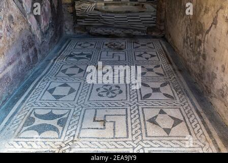 Interior of a house with its floor decorated with a mosaic of signs in the roman ruins of the ancient archaeological site of Herculaneum in Ercolano, Stock Photo