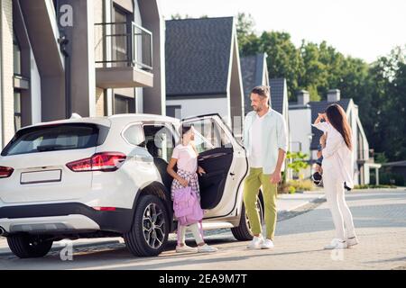 Photo portrait of daughter going to school father bringing her by car while mother watches over small boy on street in summer Stock Photo