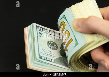 Women's hands move through a stack of hundred-dollar bills on a dark background close-up Stock Photo