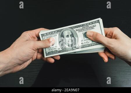 Male and female hand holding a wad of dollars on a black background close-up. Concept of bribery, assistance, and remuneration Stock Photo