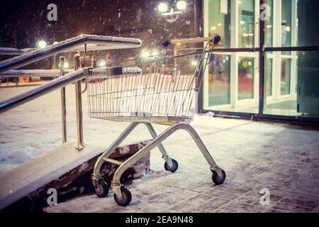 Empty shopping cart sits on the steps outside the store on a snowy winter evening Stock Photo