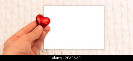Blank A5 mockup Valentine's Day theme with red heart in hand of boy, knitted sweater background, greeting card and banner photo Stock Photo