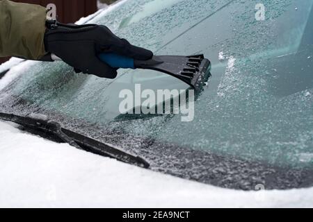 Winter scene, human hand in glove scraping ice from windshield of car Stock Photo