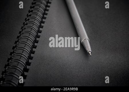 Black spiral notebook and ballpoint pen on it. Close up. Low key. Stock Photo