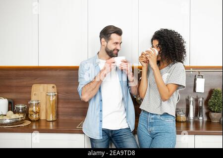 Shy young African American woman and handsome man interracial couple enjoying the happy morning together, standing leaning on the modern kitchen Stock Photo