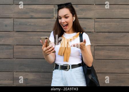 Photo of beautiful amazing amazed young woman wearing casual clothes standing in the street having communication via mobile phone looking at Stock Photo