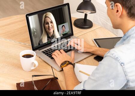 View over businessman shoulder at laptop where four multiracial colleagues engaged at group meeting on-line, video conference call communicating by Stock Photo