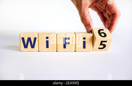 WiFi 5 or 6 symbol. Businessman turns a wooden cube and changes the words WiFi 5 to WiFi 6. Beautiful white background, copy space. Business, technolo Stock Photo