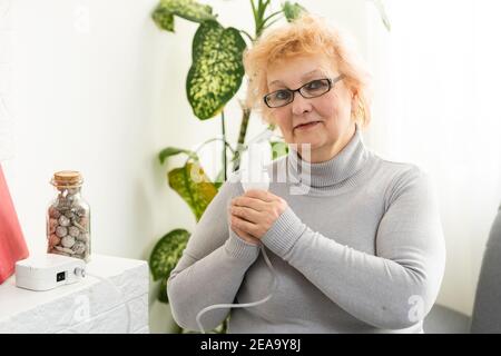 Elderly woman using asthma machine on light background Stock Photo