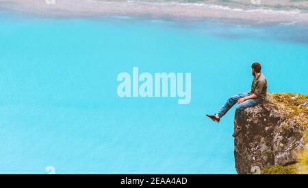 Man sitting on cliff edge travel alone looking at aerial blue sea view in Norway hiking solo outdoor healthy lifestyle summer trip Stock Photo