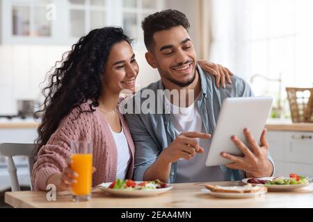 Loving Arab Couple Eating Breakfast Together And Using Digital Tablet In Kitchen Stock Photo