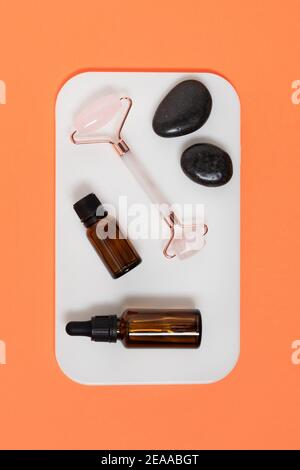 Pink quarts face massage jade roller with cosmetic oil on orange  background top view. Face care treatment. Stock Photo