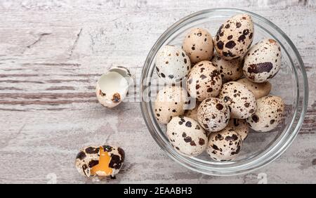 Quail eggs in a glass bowl and broken eggs on wooden table. Copy space, template, top view Stock Photo