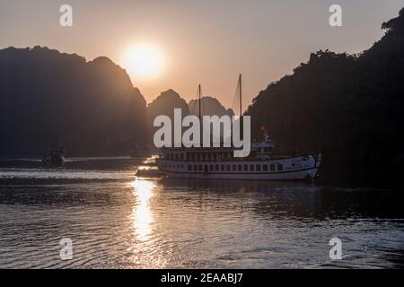 Tourist boat backlit by the rising sun, Halong Bay, Vietnam Stock Photo