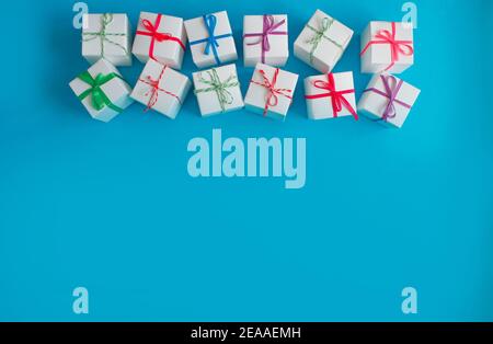 White boxes with colored ribbons lie on a blue background. Top view. Space for the text. Stock Photo