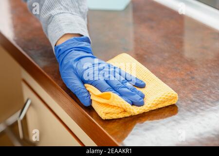 Woman wiping table countertop in kitchen by wet cloth rag. Female charwoman hand cleaning disinfect office home restaurant surfaces. Stock Photo