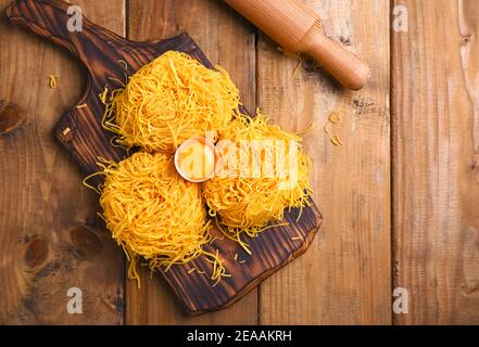 Tagliatelle pasta is thin. Traditional Italian named Angel Hair. Italian egg pasta, homemade and fresh on a wooden table. Rustic cuisine of the north of Italy. Copy space . Above Stock Photo