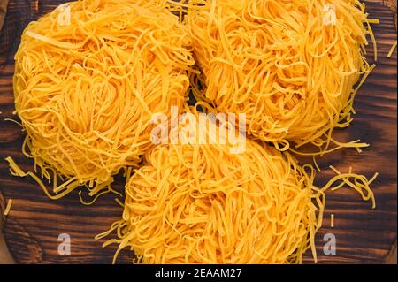 Italian egg pasta, homemade and fresh on a wooden table. Tagliatelle pasta is thin. Traditional Italian named Angel Hair. Rustic cuisine of the north of Italy . Above Stock Photo