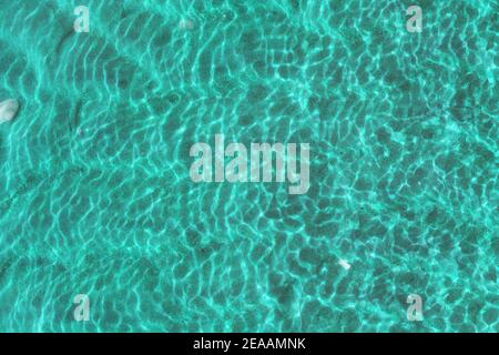 Clear water in the sea texture, sun glare, waves and sea sand at the bottom. Light blue ripples sea water background. Stock Photo