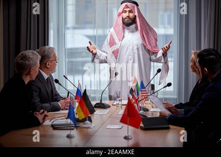 Arab Sheikh holds a meeting without ties to discuss ideas and issues on the agenda, using microphone for giving speech. in boardroom, multi-ethnic col Stock Photo