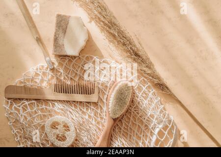 Zero waste bathroom accessories hairbrush, bamboo toothbrush, loofah and natural soap in reusable shopping bag on beige background. Top view. Vintage Stock Photo