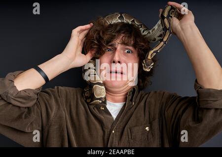 snake climbed on man's head, man is even more afraid, he feels danger, stand frightened and scared, terrified Stock Photo