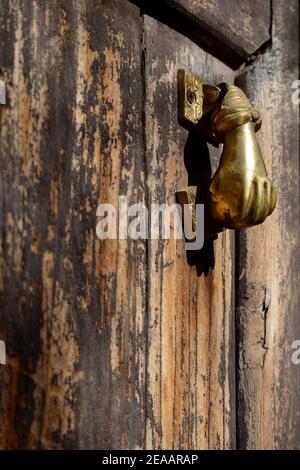 A brass door knocker in the shape of a hand on the antique weathered door of an old house in Santa Fe, New Mexico. Stock Photo