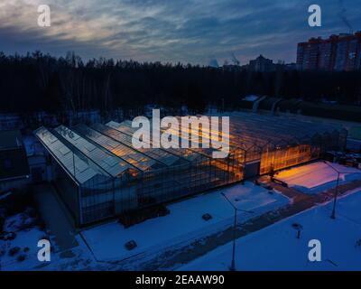 Glowing modern glass greenhouse in winter night, aerial view. Stock Photo