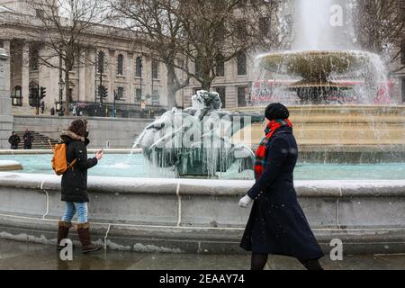 London, UK. 08 Feb 2021. UK Weather: Women view an ice covered frozen fountain in Trafalgar Square. Caused by Storm Darcy. Credit: Waldemar Sikora Stock Photo