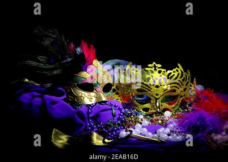 Two ornate gold masks with feathers and satin fabric sit in a colorful still life arrangement. Stock Photo