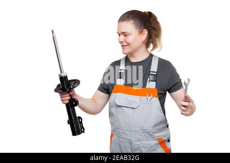 male mechanic in gray uniform with spanner wrench in pocket is looking on steel car spare part of suspension system front shock absorber isolated on w Stock Photo