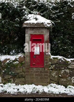 A post box mounted in a wall in a village with snow. during winter. Stock Photo